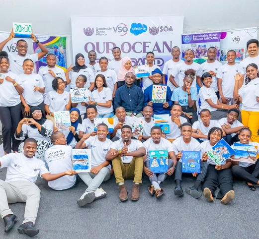 A group of approximately 30 people stands around a sign reading "our ocean" with marine-themed artwork. 
